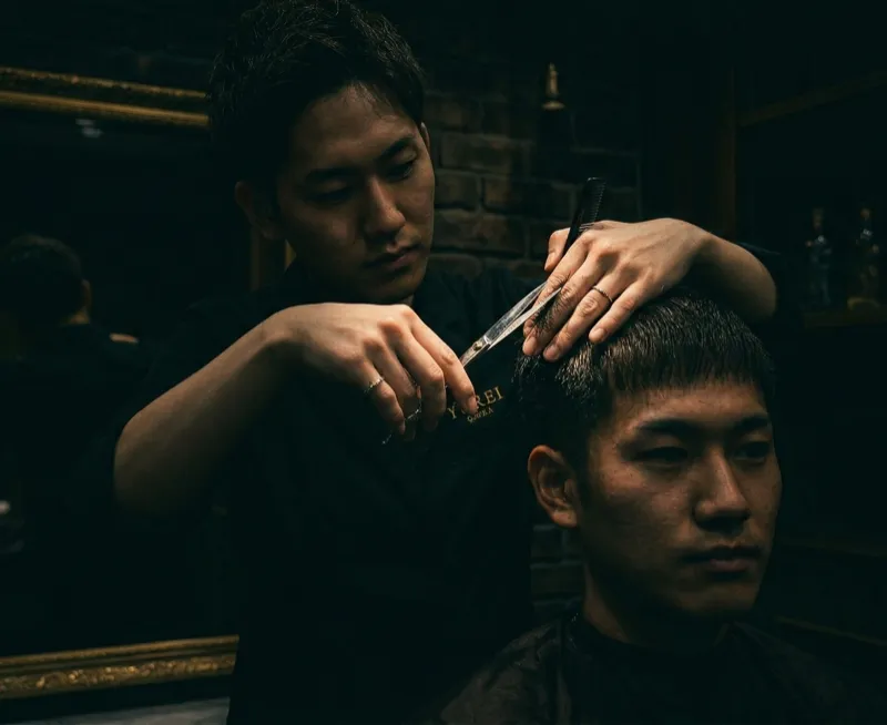 Male barber cutting customer in dark moody salon with framed artwork
