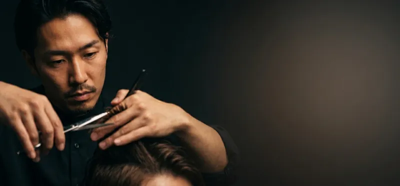 Barber hands demonstrating precision cutting technique with dark moody lighting