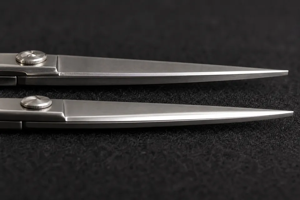 Two scissor blades shown close up on dark cloth, with different edge finishes.