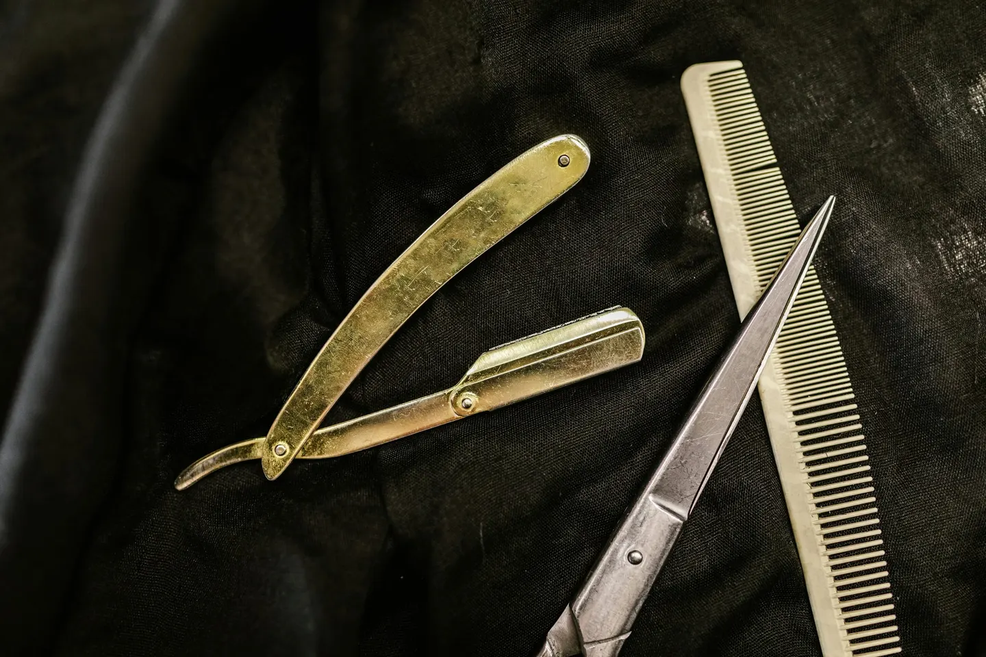 Straight razor, barber scissors and a comb laid on black cloth