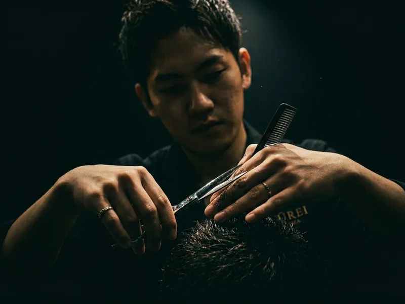 Professional barber using premium Japanese cutting scissors in a dark moody salon